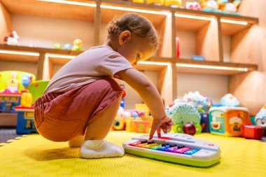 İlginç bir çocuk renkli bir oyuncak piyanoyla oynarken müzik ve öğrenme aktivitelerini parlak ve ilgi çekici oyuncaklarla dolu bir oyun odasında keşfediyor.