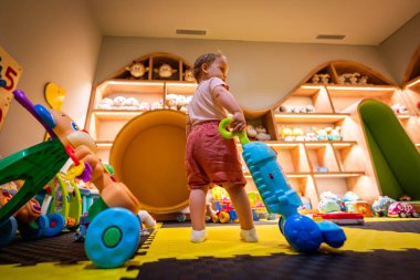 Yaratıcılık ve motor beceri geliştirme için tasarlanmış canlı ve etkileşimli bir oyun odasında oyuncak bir elektrik süpürgesi ile keşif yapan çocuk.