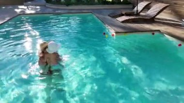 Ebeveynler ve bebekler, parlak güneş ışığı altında arka bahçede yüzme havuzunda özel anlar paylaşıyorlar.