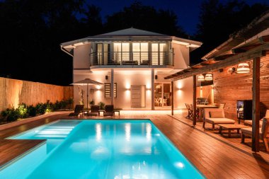 Lüks, aydınlık yüzme havuzu ve geceleri açık havuzu olan modern bir ev. Ahşap güverte ve rahat ışıklandırmayla donatılmış zarif bir arka bahçe.