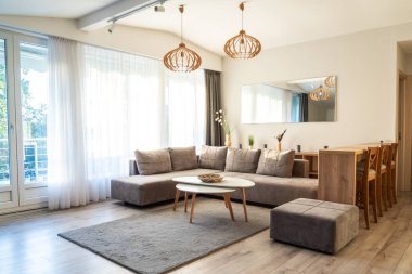 Gri bölmeli kanepesi, beyaz kahve masası, ahşap yemek takımı ve geniş pencereli parlak modern oturma odası.