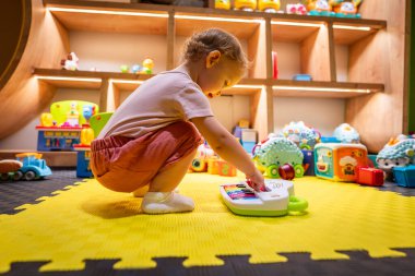 Etkileşimli öğrenme ve erken çocukluk gelişimi için tasarlanmış canlı bir oyun odasında oyuncak bir piyanoyla sesleri ve renkleri keşfeden küçük bir çocuk.