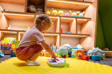 Parlak, renkli ve etkileşimli bir oyun odasında müzik ve öğrenme aktivitelerini piyano ve oyuncaklarla keşfeden çocuk