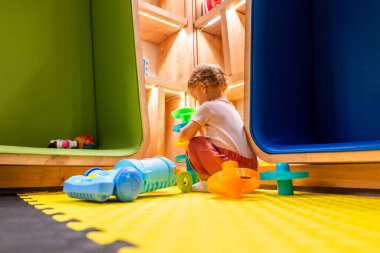 Bebek elektrikli süpürgeyle oynuyor ve parlak ve renkli bir oyun odasında rafları keşfediyor.