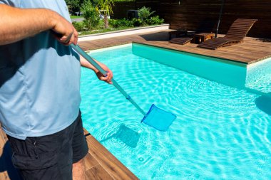 Arka bahçedeki yüzme havuzundaki turkuaz suyu temizleyen adam. Ağlı ve ahşap güverteli.