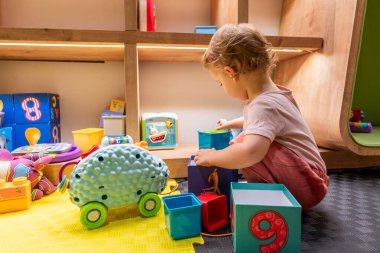 Genç çocuk renkli bloklarla oynuyor ve öğrenme alanında oyuncakları meşgul ediyor.