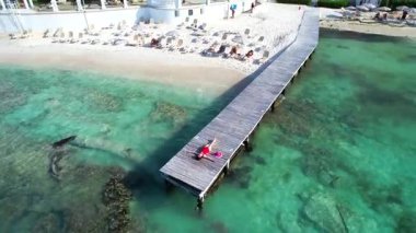Kırmızı mayo giymiş bir kadın Cancun Mexico 'daki tropik cennette turkuaz su üzerindeki ahşap iskelede dinleniyor..