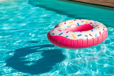 Pembe donut şeklinde, turkuaz yüzme havuzunda yüzer vaziyette, gölgesi ve ahşap güvertesi vardır.