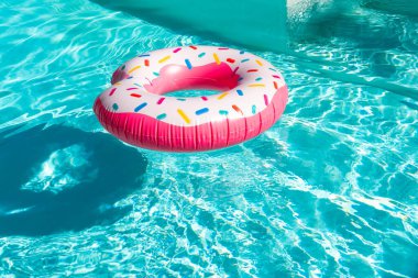 Pembe donut şekilli turkuaz yüzme havuzunda yüzen şişirilebilir bir şamandıra. Gölgesi ve güneş ışığı yansımaları var.