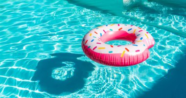 Pembe çörek turkuaz yüzme havuzunda, güneş ışığı yansımaları ve gölgelerle şişirilebilir.