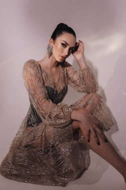 Moda stüdyosundaki fotoğrafta siyah saçlı, şık parti elbisesi ve aksesuarlarıyla güzel seksi bir kadın var.