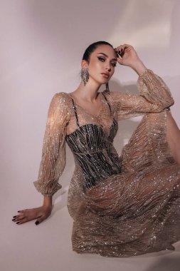 Moda stüdyosundaki fotoğrafta siyah saçlı, şık parti elbisesi ve aksesuarlarıyla güzel seksi bir kadın var.