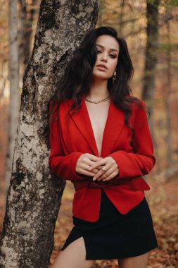 Güz ormanlarında poz veren zarif kıyafetler ve aksesuarlarla siyah saçlı güzel bir kadının moda fotoğrafı.