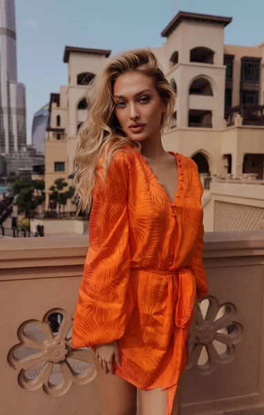 背景に高層ビルが建ち並ぶ堤防の上に立つエレガントなドレス姿の金髪の美しい女性のファッション屋外写真 — ストック写真