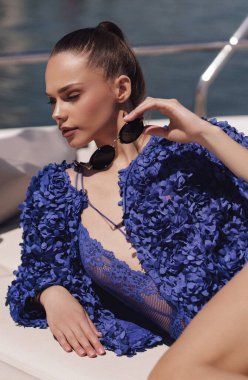 Güzel, siyah saçlı, şık elbiseli, lüks bir yatta poz veren güzel bir kadının açık hava fotoğrafı.