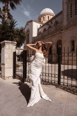 Güzel, siyah saçlı, lüks gelinlikli, tuhaf bir şehrin sokaklarında poz veren aksesuarlı güzel bir kadının moda fotoğrafı.