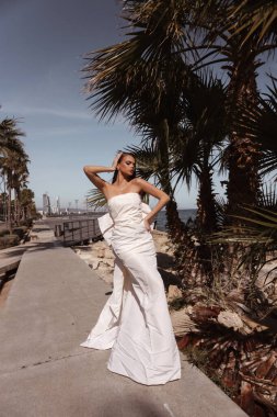 Güzel, siyah saçlı, lüks gelinlikli, tuhaf bir şehrin sokaklarında poz veren aksesuarlı güzel bir kadının moda fotoğrafı.