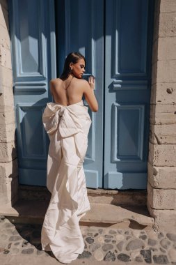 Güzel, siyah saçlı, lüks gelinlikli, tuhaf bir şehrin sokaklarında poz veren aksesuarlı güzel bir kadının moda fotoğrafı.