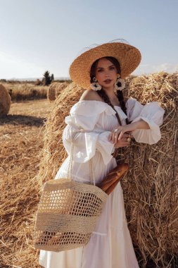 Güzel, siyah saçlı, zarif beyaz elbiseli ve samanlıkta poz veren güzel bir kadının moda fotoğrafı.