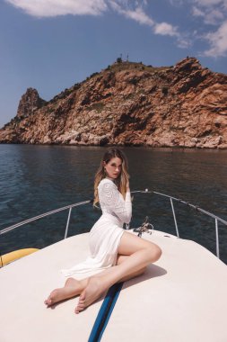 Koyu renk saçlı, beyaz elbiseli güzel bir kadın yatın güvertesinde dinleniyor, Akdeniz 'de yelken açıyor.