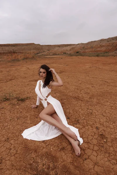 キプロスの砂漠でポーズをとるアクセサリーと豪華な白いドレスで暗い髪の美しい女性のファッション屋外写真 — ストック写真