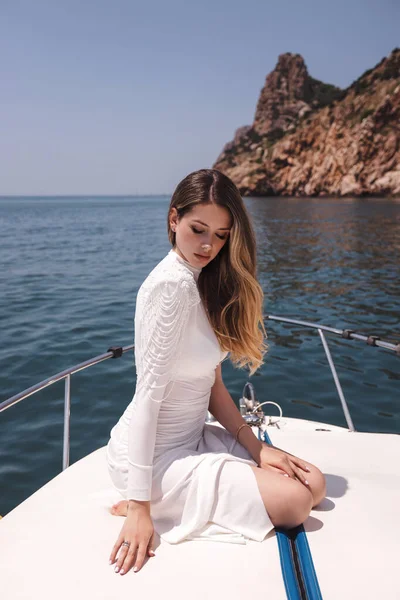 在游艇甲板上轻松自在地坐着 在静海中航行的漂亮女人 深色头发 身穿华丽的白衣 — 图库照片
