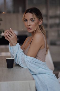 Güzel, sarı saçlı, zarif ev kıyafetleri içinde, mutfakta kahve içen güzel bir kadının moda fotoğrafı.