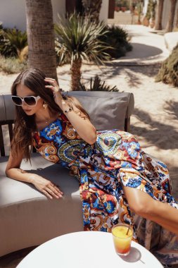 Açık hava plaj kulübünde poz veren koyu renk saçlı ve aksesuarlı güzel bir kadının moda fotoğrafı.