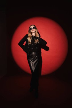 Stüdyoda poz veren sarı saçlı, lüks deri etekli ve güneş gözlüklü güzel bir kızın moda fotoğrafı.