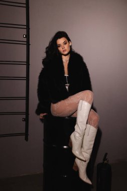 Şık kürklü, siyah saçlı ve beyaz çizmeli güzel bir kadının moda fotoğrafı.