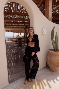 Koyu renk saçlı, şık elbiseli, yaz plaj kulübünde poz veren güzel bir kadının moda fotoğrafı.