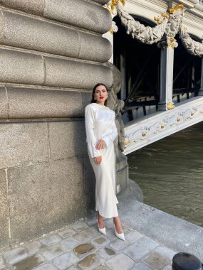 Paris 'teki Alexandre III köprüsünde poz veren siyah saçlı, beyaz ipekli ve aksesuarlı güzel bir kadının moda fotoğrafı.