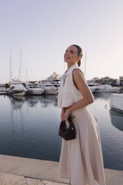 Kıbrıs 'ta yatlarla marinada poz veren zarif klasik elbiseli, koyu renk saçlı güzel bir kadının moda fotoğrafları.