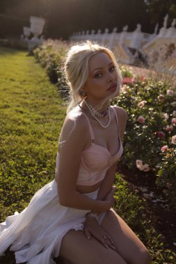 Güzel, şehvetli, sarışın, zarif elbiseli, aksesuarlı ve bahçeli güzel bir villada poz veren güzel bir kadının moda fotoğrafı. 