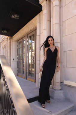 Güzel, siyah saçlı, şık siyah elbiseli ve güzel villada poz veren aksesuarlı güzel bir kadının moda fotoğrafı.