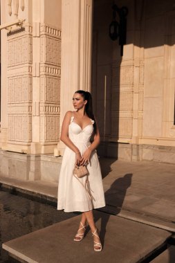 Güzel, açık hava fotoğrafında siyah saçlı, lüks elbiseli, aksesuarlı güzel bir villada klasik tarzda poz veren güzel bir kadın.