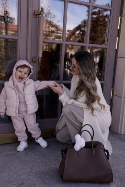 Güzel bir ailenin moda fotoğrafı: uzun sarı saçlı anne rahat beyaz bir palto giyiyor küçük oğluyla sokakta yürüyor
