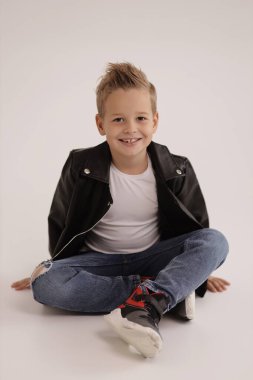 Stüdyoda poz veren sarı saçlı, deri ceketli ve kot pantolonlu hoş bir çocuğun moda fotoğrafı.