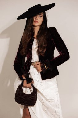 Siyah ceketli, siyah ve büyük yuvarlak şapkalı, siyah kıvırcık saçlı, güzel Slav bir kadının moda fotoğrafı. Stüdyoda poz veriyor.