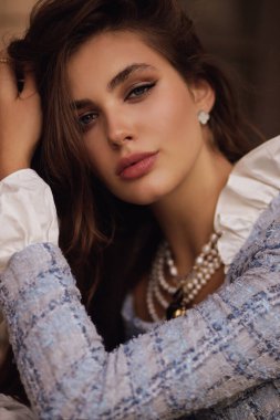 Koyu kıvırcık saçlı güzel bir kadının açık hava fotoğrafı zarif mavi tüvit ceket takıyor ve kafede poz veriyor.