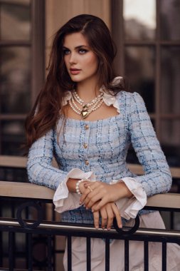 Koyu kıvırcık saçlı güzel bir kadının açık hava fotoğrafı zarif mavi tüvit ceket takıyor ve kafede poz veriyor.