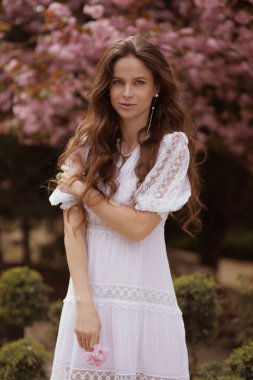 Güzel bir açık hava fotoğrafı. Uzun doğal saçlı, zarif elbiseli, çiçek açan Sakura bahçesinde poz veren güzel bir kadın.