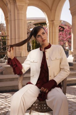 Güzel, siyah saçlı, zarif elbiseli ve çiçek açan ağaçlarla bahçede poz veren güzel bir kadının açık hava fotoğrafı.