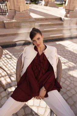 Güzel, açık hava fotoğrafında siyah saçlı, zarif elbiseli ve tuhaf bir bahçede poz veren genç bir kadın.