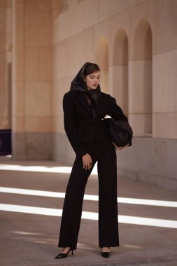Uzun siyah saçlı, şık siyah takım elbiseli, şık, antika bir villada poz veren güzel bir kadının moda fotoğrafı.