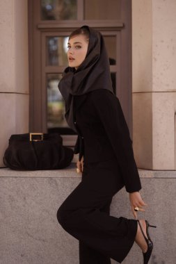 Uzun siyah saçlı, şık siyah takım elbiseli, şık, antika bir villada poz veren güzel bir kadının moda fotoğrafı.