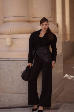 Uzun siyah saçlı, şık siyah takım elbiseli, şık, antika bir villada poz veren güzel bir kadının moda fotoğrafı.