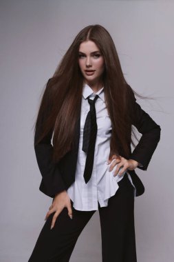 Moda stüdyosu fotoğrafı. Uzun siyah saçlı, zarif, erkeksi takım elbiseli ve kravatlı güzel bir kadın.