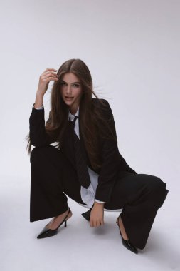 Moda stüdyosu fotoğrafı. Uzun siyah saçlı, zarif, erkeksi takım elbiseli ve kravatlı güzel bir kadın.