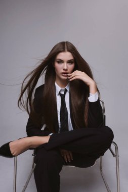 Moda stüdyosu fotoğrafı. Uzun siyah saçlı, zarif, erkeksi takım elbiseli ve kravatlı güzel bir kadın.